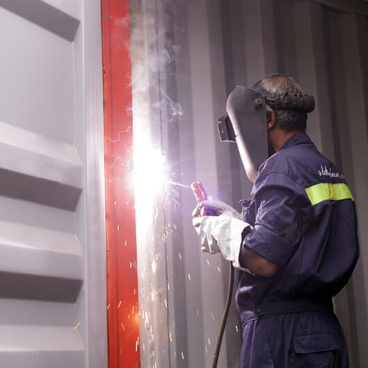 A skilled worker repairing and rigging shipping containers.