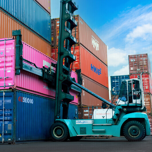 A container stacker crane lifting up stacking container boxes in yard